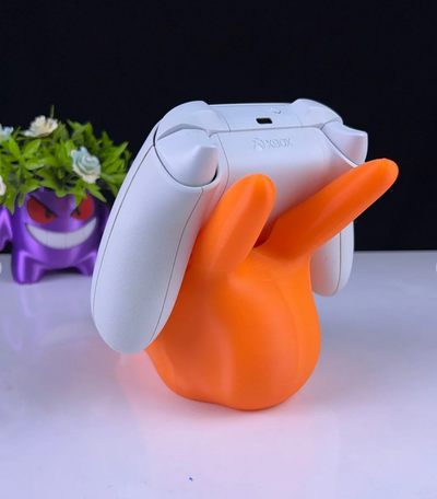 3DPrintingLabDesigns orange Charizard controller stand holding a white Xbox controller with a Gengar planter nearby.