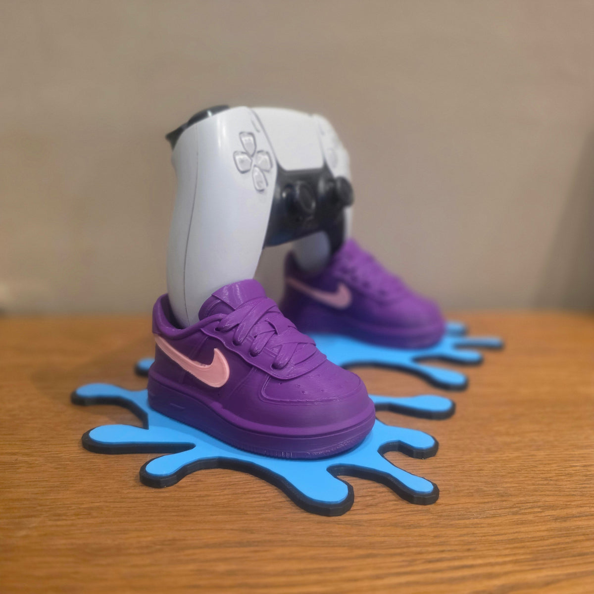 3DPrintingLabDesigns sneaker-inspired purple and pink PS5 controller stand on a blue drip base on a wooden desk