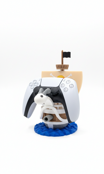 One Piece Going Merry PS5 DualSense controller stand and dock. The stand is a colorful replica of the Going Merry ship sailing on blue ocean waves, securely holding a white PlayStation 5 controller.