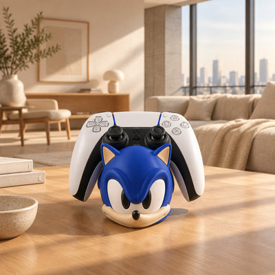 A blue Sonic the Hedgehog head-shaped stand holding a white and black PlayStation 5 controller, set on a wooden tabletop with a blurred indoor background.
